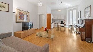A modern living room with a flat-screen TV, a glass coffee table, and a sofa. There is a dining area with a piano and a kitchen in the background. - Central Milan Apartment - 10 min Duomo (Milan)