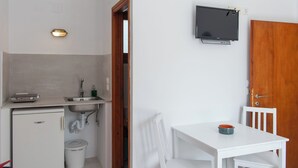 A compact kitchen with a sink, a small refrigerator, and a television mounted on the wall. - Blue Fish (Sifnos)