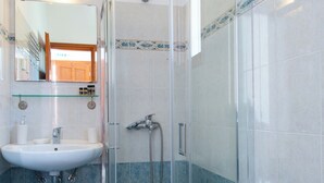 A bathroom with a glass-enclosed shower, a sink, and a toilet. - Blue Fish (Sifnos)