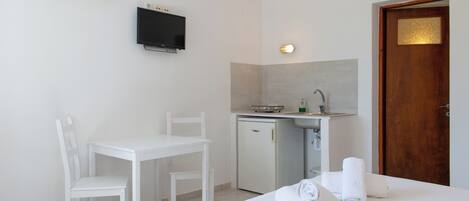 A small, clean room with a bed, a desk, a chair, a TV, a sink, and a door.