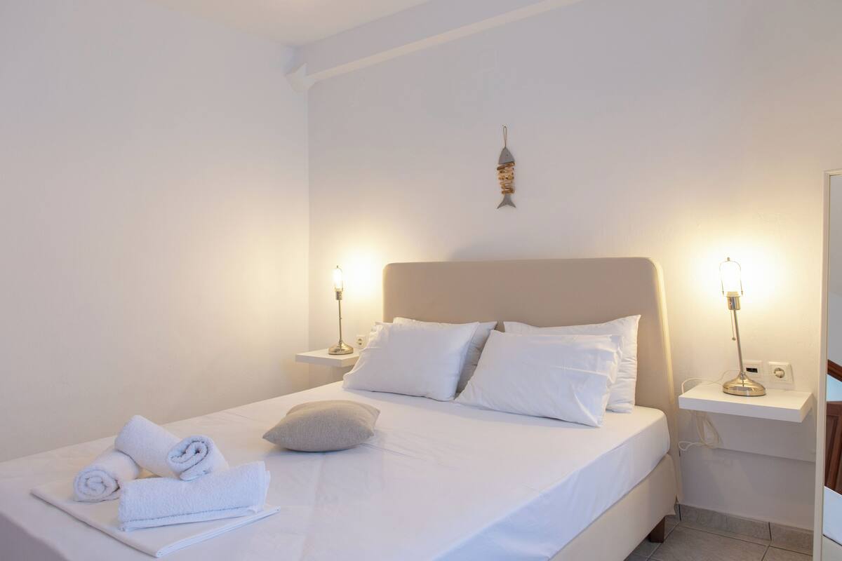 Un letto rifatto con lenzuola e cuscini bianchi, due comodini con lampade e un lampadario a parete.