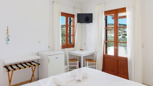 A room with a bed, a desk, a chair, a TV, and a window with curtains. - Blue Fish (Sifnos)