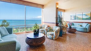 A spacious living area with a large window overlooking the ocean, furnished with a sofa, chairs, and a coffee table. - SUMMER SALE! Oceanfront 1BD Condo with Sunset & Whale Views - Royal Kahana 1206 (Lahaina)