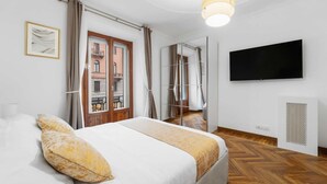 Een slaapkamer met een bed, een televisie, een raam met gordijnen en uitzicht op de straat.