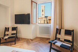 A room with a television, two chairs, a radiator, and a window with a view of a tower. - Apartments Florence - The Four Suites (Firenze)