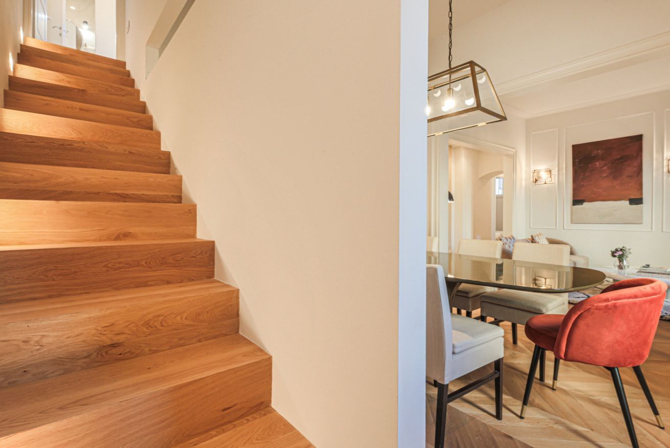 Una escalera de madera que lleva a un comedor con una mesa y sillas de vidrio.