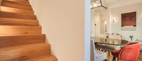 Una escalera de madera que lleva a un comedor con una mesa y sillas de vidrio.