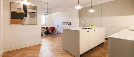 A modern kitchen with a central island, pendant lighting, and a herringbone floor pattern.
