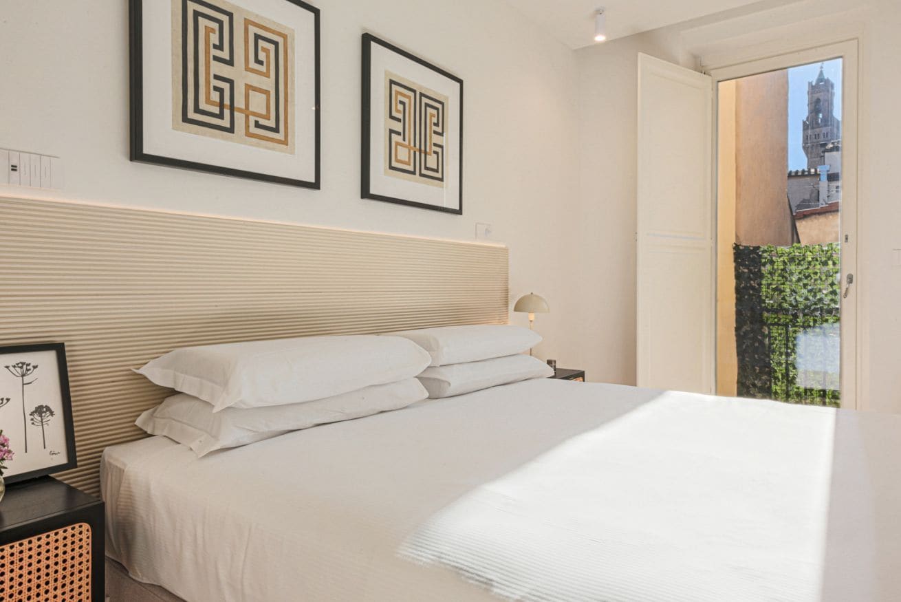 A neatly made bed with white linens, a headboard, and two framed geometric wall art pieces.