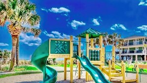 A beach playground with slides and a climbing structure, palm trees, and a building in the background. - Z35 Absolutely beautiful 2 bedroom 2 bath Ocean Lakes! (Myrtle Beach)