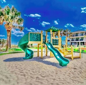 A beach playground with slides and a climbing structure, palm trees, and a building in the background. - Z35 Absolutely beautiful 2 bedroom 2 bath Ocean Lakes! (Myrtle Beach)