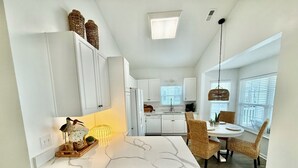 A modern kitchen with white cabinets, a marble countertop, and a dining area with wicker chairs. - Z35 Absolutely beautiful 2 bedroom 2 bath Ocean Lakes! (Myrtle Beach)