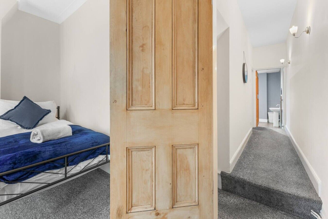 A hotel room with a bed, a wooden door, and a staircase leading to a bathroom.