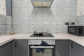 A modern kitchen with a tiled backsplash, a stove, a microwave, and a built-in oven. - Stoke Work Stay - Contractors & Families - Sleep 6 (Stoke-on-Trent)