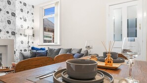 A dining area with a wooden table, grey plates, and a window with a view of a building. - Stoke Work Stay - Contractors & Families - Sleep 6 (Stoke-on-Trent)
