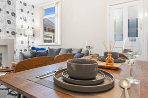 A dining area with a wooden table, grey plates, and a window with a view of a building. - Stoke Work Stay - Contractors & Families - Sleep 6 (Stoke-on-Trent)
