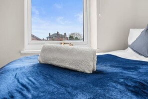 Un lit avec une couverture bleue et une serviette blanche posée dessus.