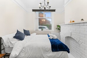 A bedroom with a bed, a window, a fireplace, and a chandelier. - Stoke Work Stay - Contractors & Families - Sleep 6 (Stoke-on-Trent)