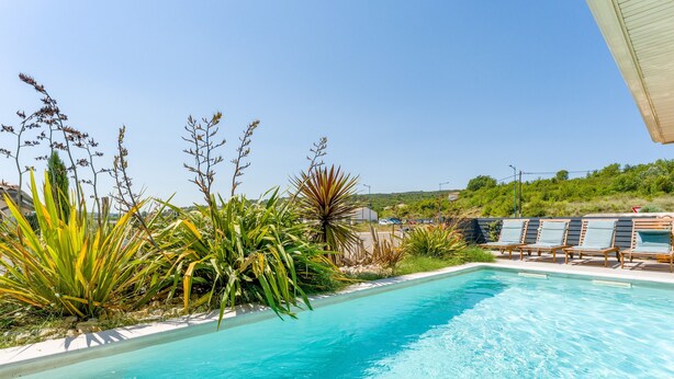 Una piscina con lettini, circondata da diverse piante.