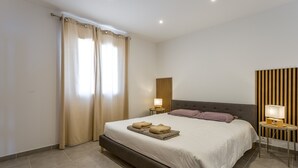 Una camera da letto con un letto, tende, un comodino con una lampada, un pannello a parete e una testiera.