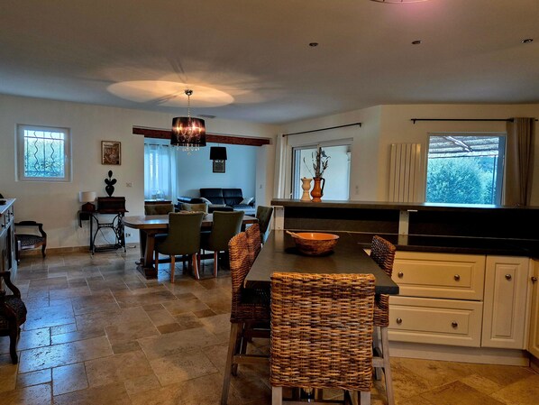A spacious living area with a dining table, chairs, a sofa, and a kitchen area with cabinets and a window.