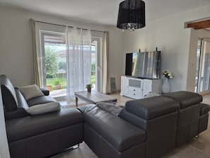 A modern living room with a sectional sofa, a flat-screen TV, and a dining area.
