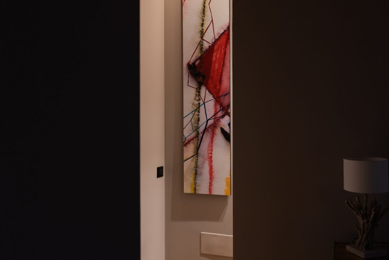 A hallway with a wall-mounted abstract painting and a lamp on a side table.