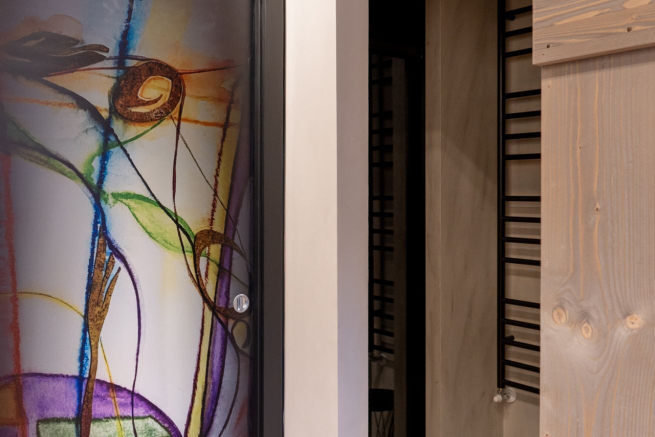 Een kamer met een houten deur en een glazen wand met abstracte kunst.