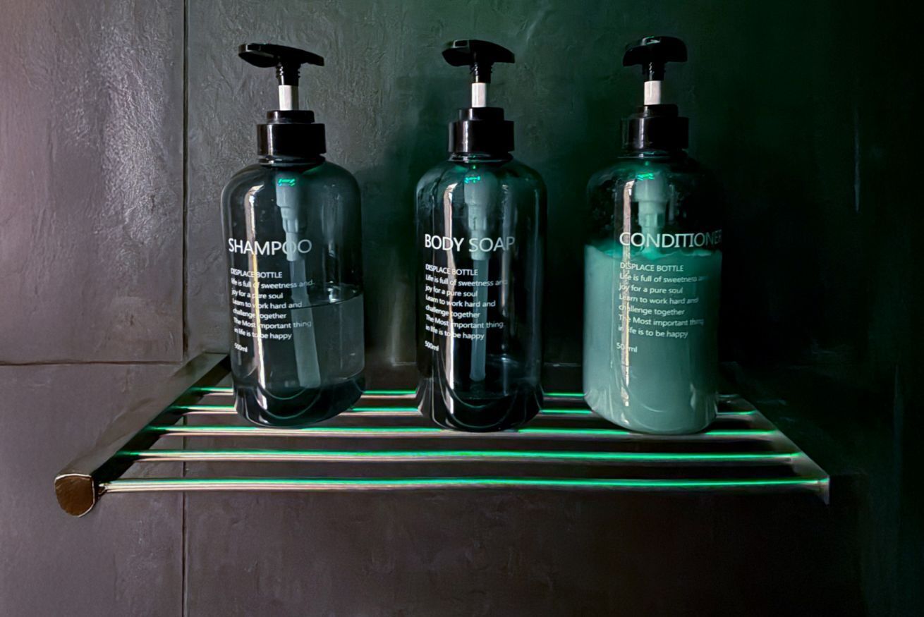 Trois bouteilles de shampoing, de savon pour le corps et d’après-shampoing sont posées sur une étagère.