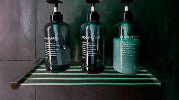 Trois bouteilles de shampoing, de savon pour le corps et d’après-shampoing sont posées sur une étagère.