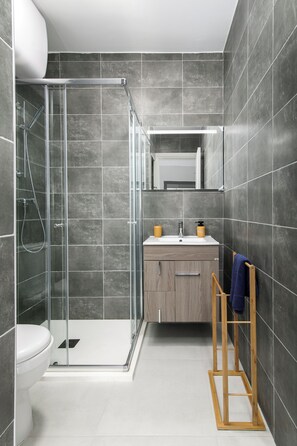 Een moderne badkamer met een glazen douchecabine, een toilet, een wastafel met spiegel erboven en een houten handdoekrek.