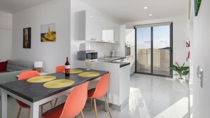 Eine moderne Küche mit weißen Schränken, ein Essbereich mit Tisch und Stühlen sowie eine große Schiebeglastür, die auf einen Balkon führt.