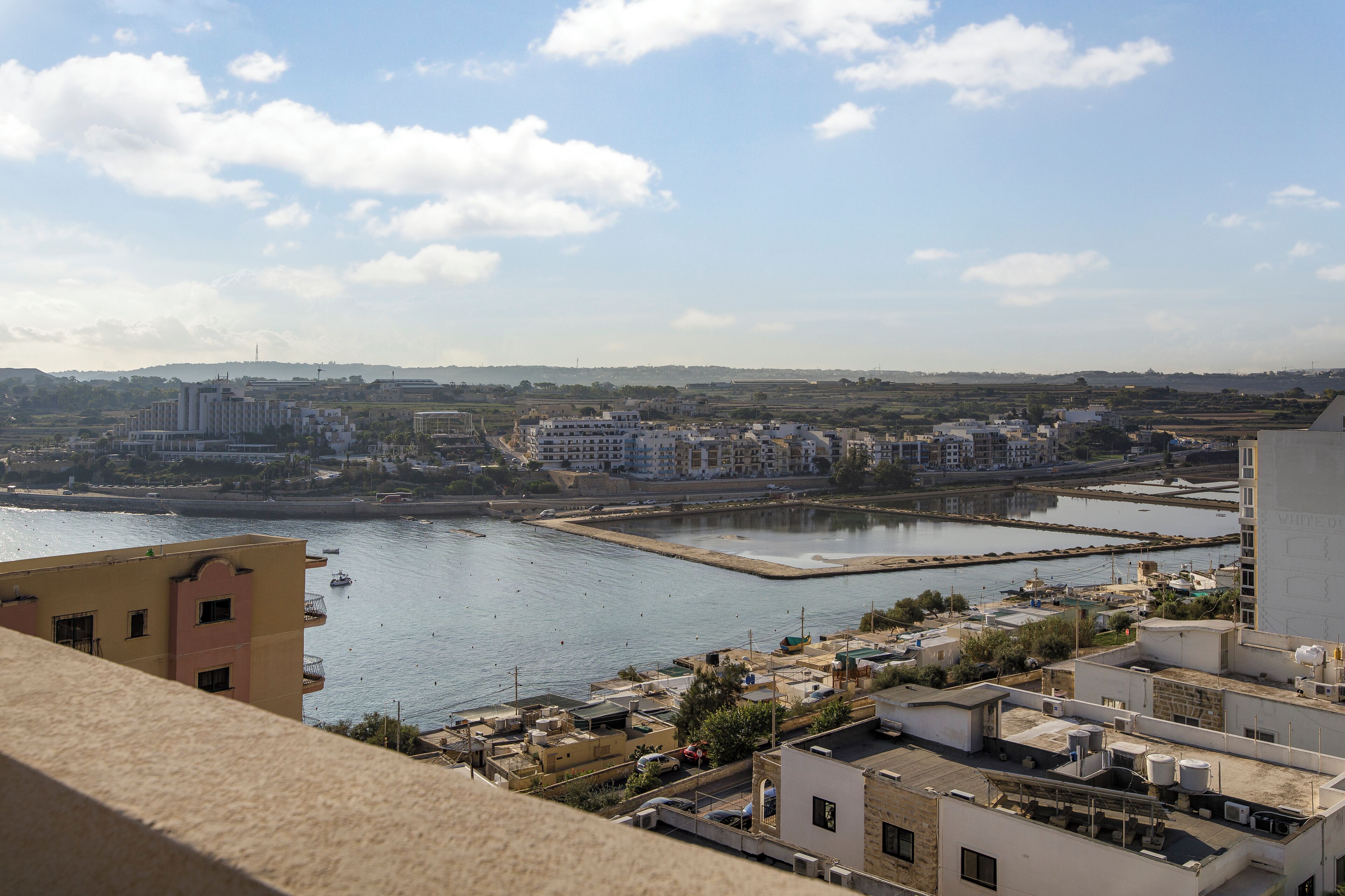Paisagem costeira urbana com edifícios ao longo da orla, um porto de iates e céu claro.