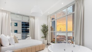 A modern bedroom with a large bed, a bathtub, and a city view through large windows. - LUX  The Sky Dubai Eye View Suite (Dubai)