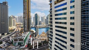 A high-rise building with a modern design, situated in a bustling urban area with other tall buildings and a body of water in the background. - LUX  The Sky Dubai Eye View Suite (Dubai)