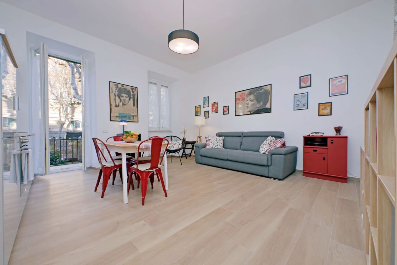 A modern living room with a grey sofa, red chairs, a dining table with fruit, and a red cabinet.