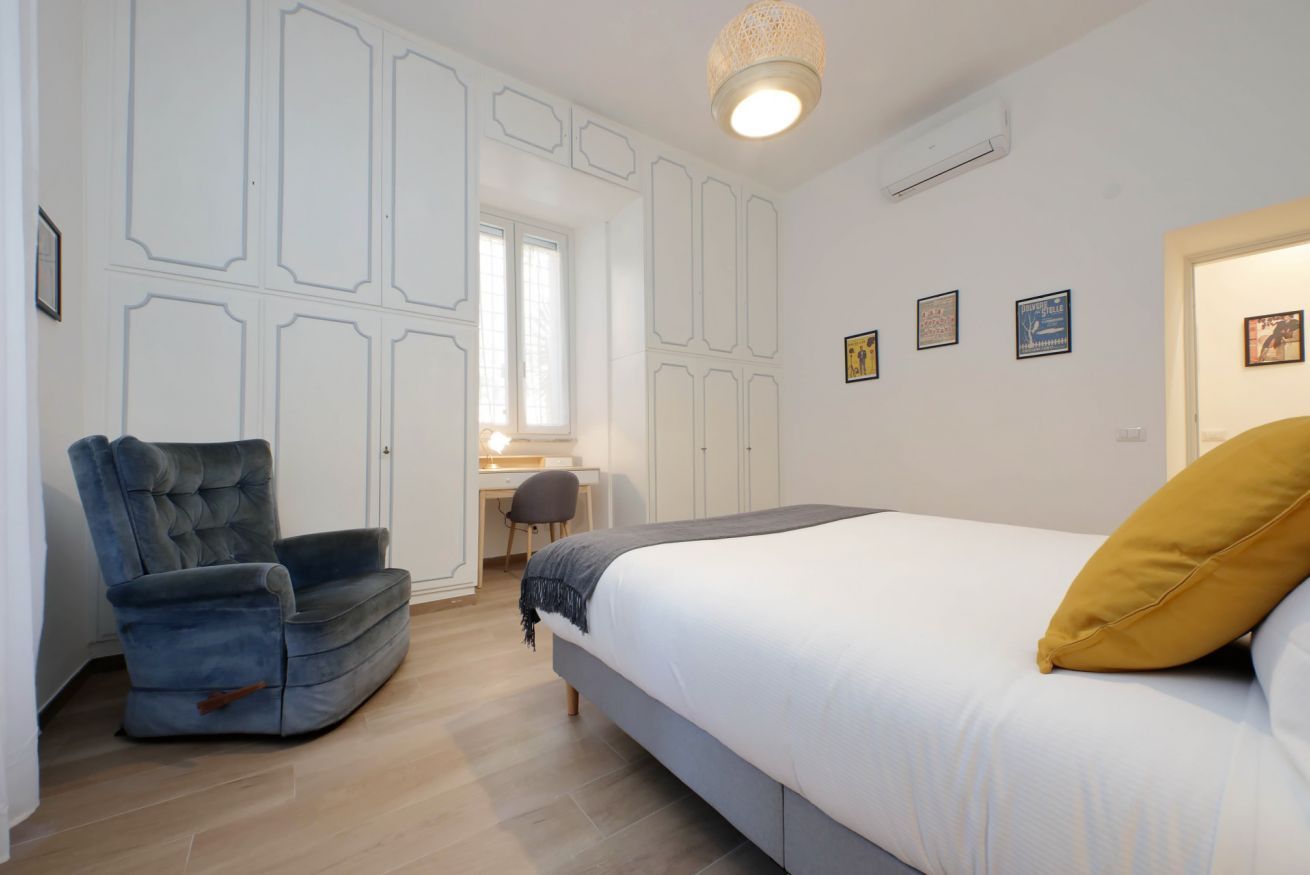 A bedroom with a bed, a chair, a desk, and a window.