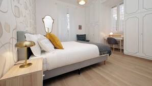 Ett sovrum med en säng, ett sängbord, en lampa, en spegel och ett skrivbord med en stol.