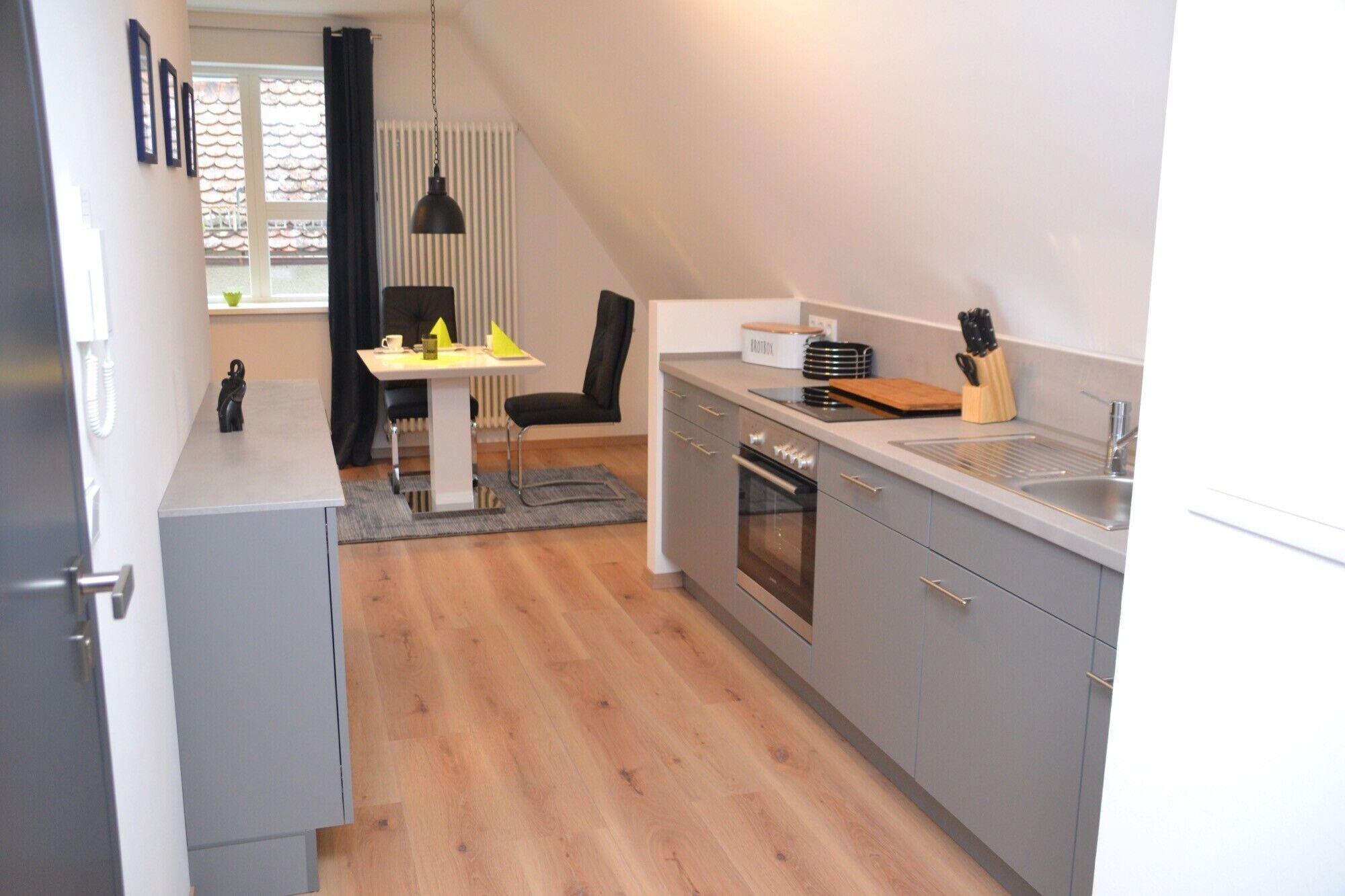 A modern kitchen with grey cabinets, a stainless steel sink, and a dining area with a table and chairs.