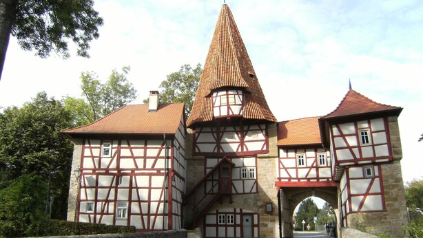 Um edifício tradicional em estilo de enxaimel com uma torre imponente, uma entrada em arco e um caminho pavimentado que leva a ele.