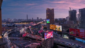 A cityscape at dusk with a prominent hotel featuring a lit sign, surrounded by busy roads and construction cranes. - StayBee - The Artists Gateway Room DownTown Cairo 5mins from Egyptian museum (cairo)