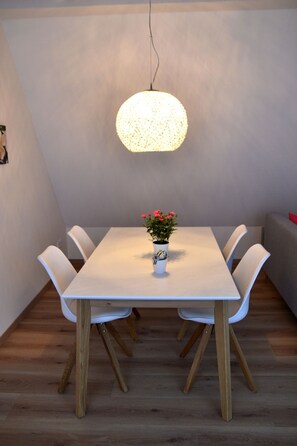 Ein Essbereich mit einem weißen Tisch, weißen Stühlen, einer Pendelleuchte und einem Blumentopf mit Blumen.
