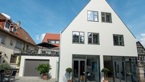 Ett modernt hus i två våningar med garage, stora glasdörrar och krukväxter.