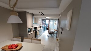 Ett modernt kök med vita skåp, en matplats med ett vitt bord och stolar, och utsikt över vardagsrummet.
