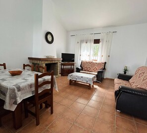 A living room with a fireplace, a dining area with a table and chairs, a sofa, and a television. - Charming Rural House With Pool in Conil (Conil de la Frontera)