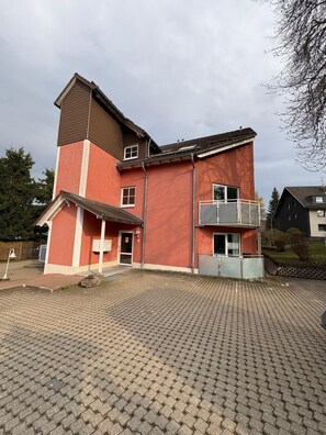 Um edifício de vários andares com fachada vermelha, varanda no segundo pavimento e entrada com calçada.