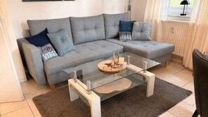Un salon moderne avec un canapé gris, une table basse en verre et un tapis marron.