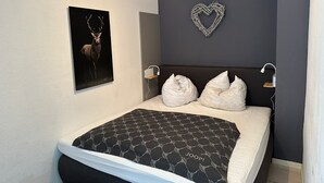 Une chambre à coucher avec un lit, un décor en forme de cœur accroché au mur, une image de cerf et une lampe de chevet.