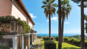A building with a stone pathway leading to a balcony overlooking a lush garden and the sea. - Villa with pool and breathtaking view - DiCasaInSicilia (Santa Venerina)