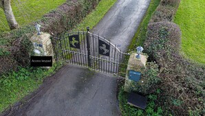 Una entrada cerrada con un portón de metal, pilares de piedra y una pequeña lámpara en la parte superior.
